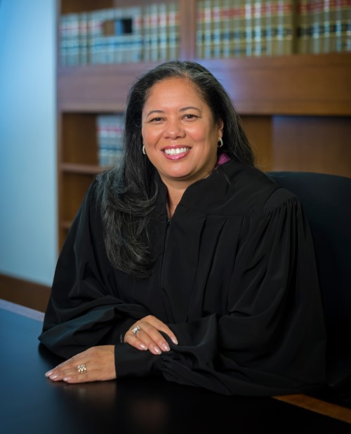 Black and Asian American woman with long dark hair and gray streaks sitting in black judge's robes, Judge Angel Kelley