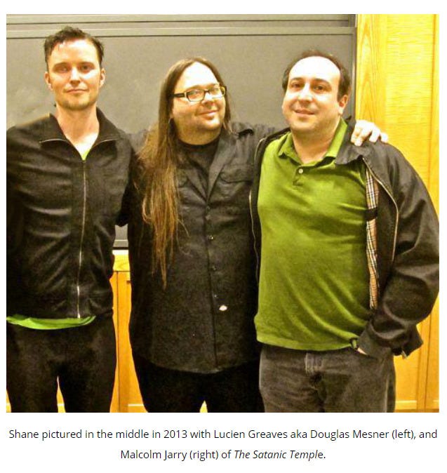 image of three white men standing together. Caption: "Shane [Bugbee] pictured in the middle in 2013 with Lucien Greaves aka Douglas Mesner (left), and "Malcolm Jarry (right) of The Satanic Temple." However, "Lucien Greaves" and "Mesner" are pseudonyms for Douglas Alexander Misicko and "Malcolm Jarry" is a pseudonym for Cevin Soling
