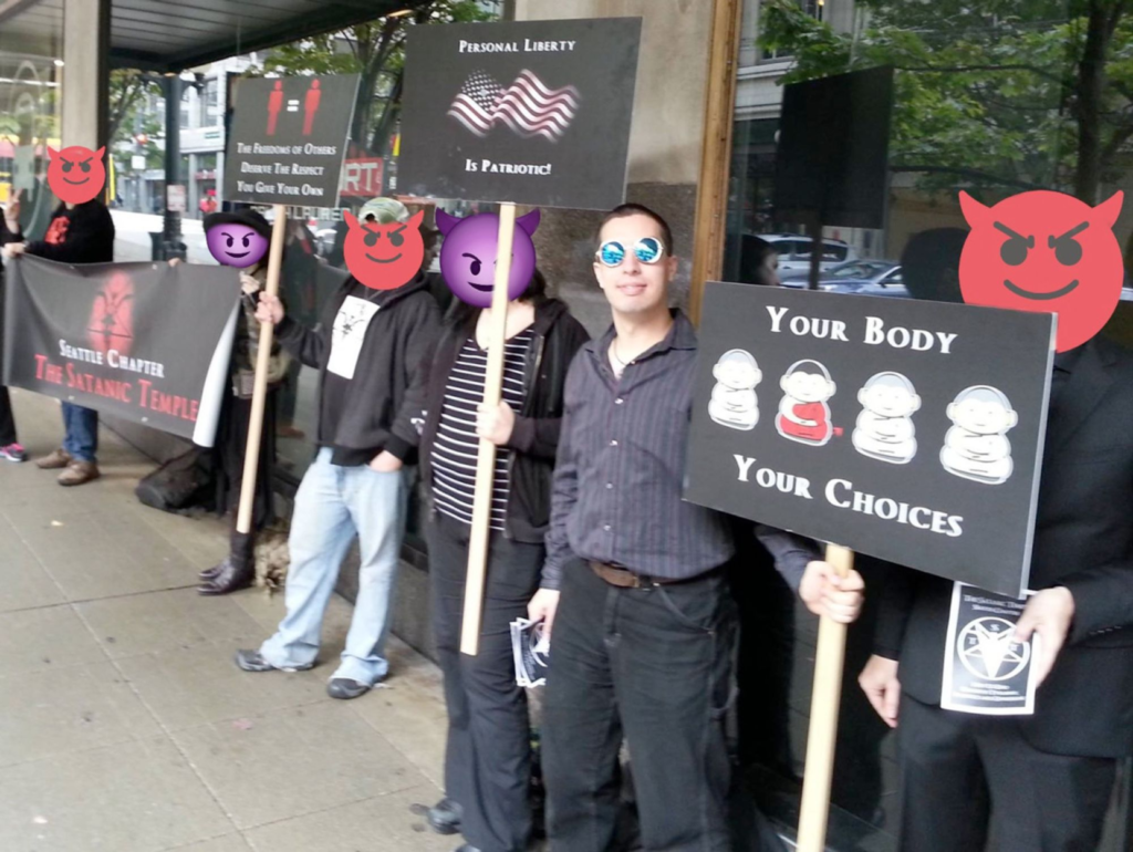 Nathan Sullivan standing with a "your body, your choices" sign during a Satanic Temple public action circa 2017