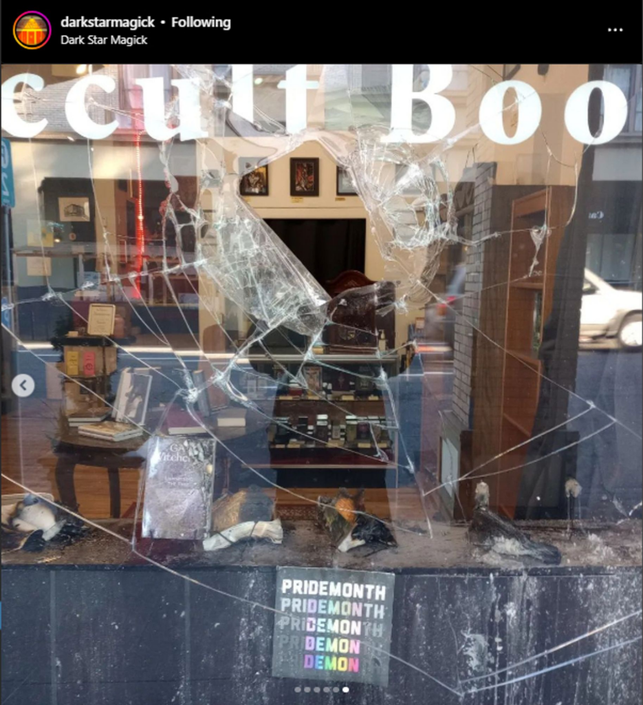 screenshot of @DarkStarMagick instagram post of broken storefront window and burnt books with "pride month" to "demon" type sitting intact in front of it